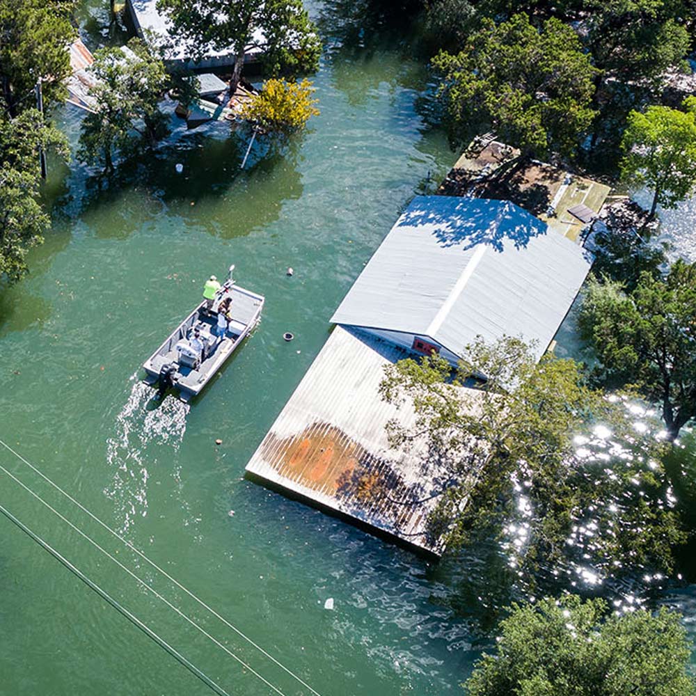 Image from above of houses flooded and a boat searching for people.