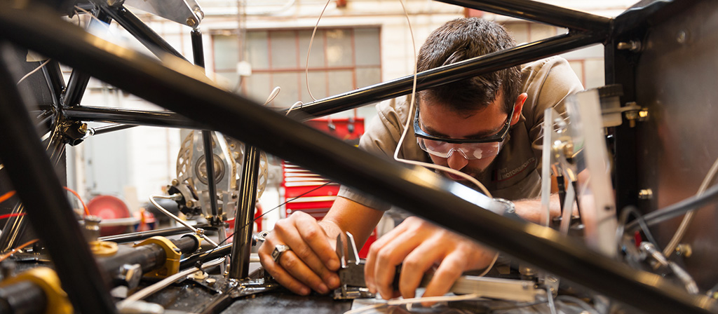 A student works with his hands on a machine made of pipes and gears